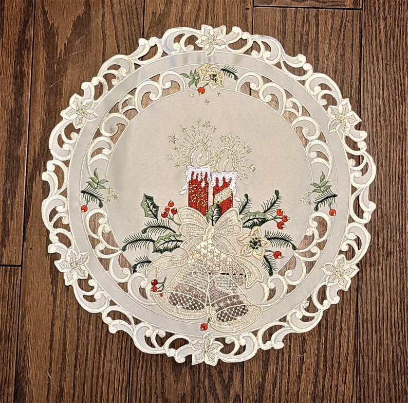 Puede incluir: Camino de mesa de encaje blanco con un delicado dise&ntilde;o floral y un tema navide&ntilde;o. El dise&ntilde;o presenta velas rojas y blancas, campanas y acebo.