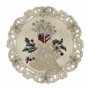 Puede incluir: Un mantel individual redondo de encaje blanco con un dise&ntilde;o bordado de dos campanas doradas, una vela roja con detalles dorados y un lazo dorado. El dise&ntilde;o est&aacute; rodeado de hojas verdes y bayas rojas.