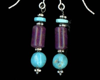 May include: A pair of dangle earrings with silver hooks. Each earring features a turquoise bead, a purple cylindrical bead, and a turquoise disc. The earrings are suspended from silver hooks, creating a simple yet elegant design.