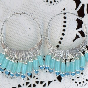 May include: Silver hoop earrings with a textured crescent design and dangling turquoise-colored beads. The earrings have a delicate, bohemian style, perfect for adding a touch of color and flair to any outfit.