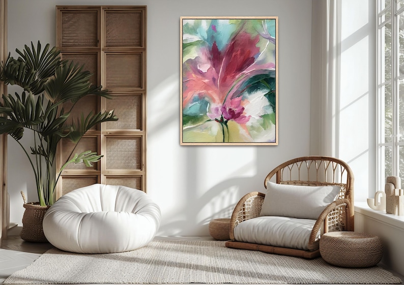Pu&ograve; includere: Dipinto floreale astratto in cornice dorata su parete bianca. L'opera presenta un grande fiore stilizzato con sfumature di rosa, rosso e verde. Un pouf bianco e una sedia in vimini con cuscino sono nella stanza.
