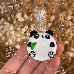 Peut inclure: Une broche ronde panda blanche et noire avec une petite tige de bambou verte. Elle comporte le texte : little panda, big joy, so cute!, tiny details make me happy, et a little piece of happiness, ainsi que des icônes de cœurs et d'étoiles.