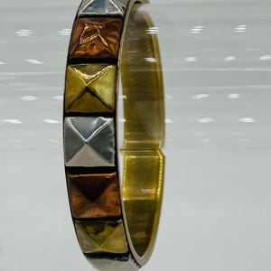 May include: A gold bangle bracelet with a row of pyramid-shaped studs in silver, copper, and gold.