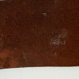 Puede incluir: Primer plano de un cintur&oacute;n de cuero marr&oacute;n. El cintur&oacute;n tiene una superficie texturizada con algunas manchas m&aacute;s claras. Los bordes del cintur&oacute;n son de color marr&oacute;n oscuro. El fondo es blanco.