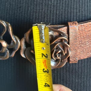 Wide dark brown leather belt with a large, sculptural double-rose copper buckle