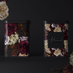 May include: Two black metal canisters with floral designs. The canisters have a dark background with burgundy, cream, and purple flowers. The canister on the right has the text "Autumnal Floral Collection" on a black label.