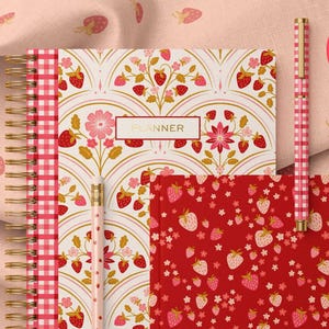 May include: A collection of stationery items with a strawberry theme. Includes a spiral-bound planner, a notebook, a pencil, and a pen. The planner and pencil have a floral and strawberry design, while the notebook features a red strawberry pattern. The pen has a pink and white checkered pattern.