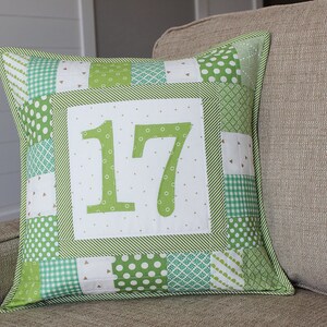 May include: Green and white patchwork pillow with the number 17 in the center. The pillow is made of different green fabrics with white polka dots, gingham, and stripes.