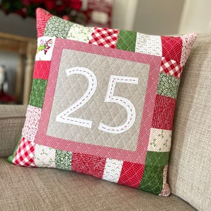 May include: A red, green, and white patchwork pillow with the number 25 stitched in white on a beige background.