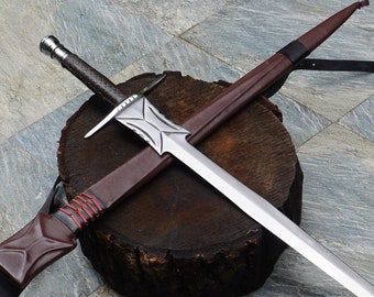 May include: A silver sword with a brown leather scabbard. The sword is lying on a wooden log with the scabbard resting on top of it.