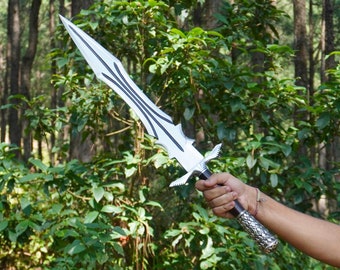 May include: A silver sword with a black handle and a decorative design. The sword is held by a person's hand in a forest setting.