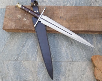 May include: A silver dagger with a brown wooden handle and a leather sheath. The dagger is lying on a wooden board.