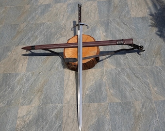 May include: A silver sword with a brown leather scabbard. The sword is resting on a wooden log with the scabbard lying across it.