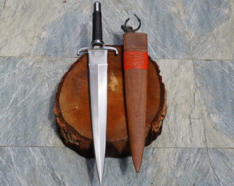 May include: A silver dagger with a black handle and a leather sheath with red stitching. The dagger and sheath are resting on a wooden surface.