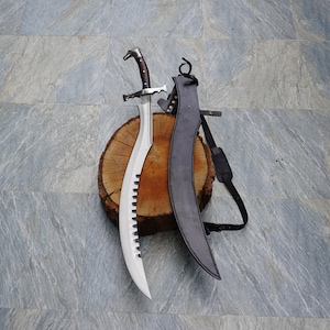 Op de afbeelding: Een zilveren zwaard met een zwarte leren schede. Het zwaard heeft een gebogen lemmet en een decoratief handvat. De schede heeft een riem om te dragen.