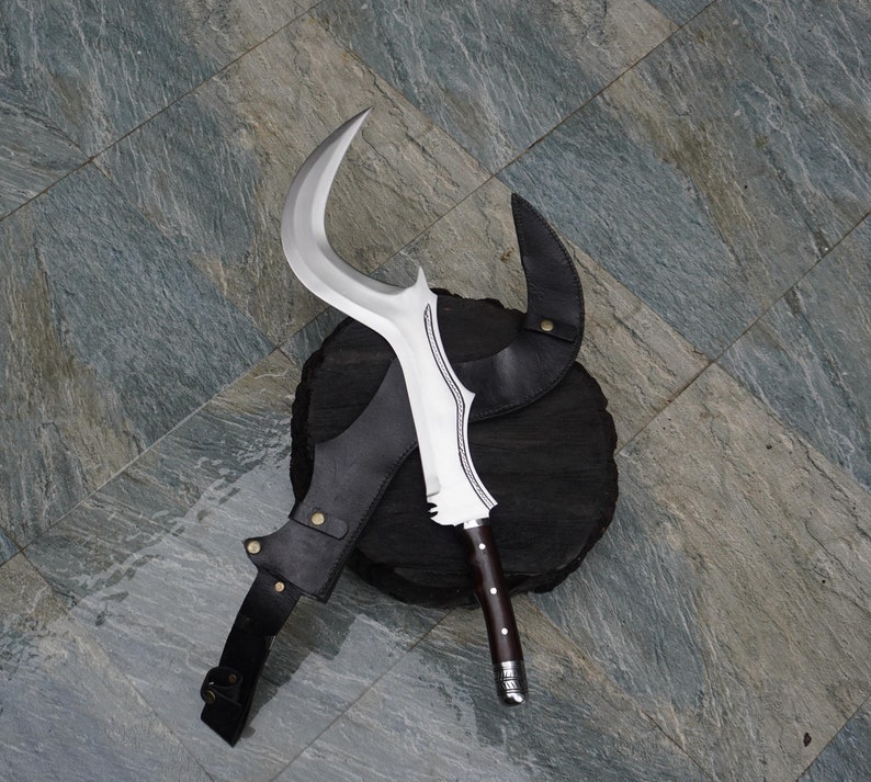 Puede incluir: Una hoja curva plateada con una funda de cuero negro. La hoja est&aacute; sobre una base de madera negra.
