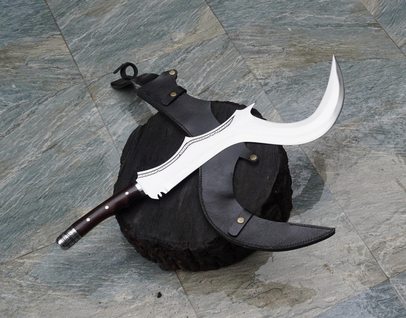 Puede incluir: Un cuchillo curvo de color plateado con mango de madera y funda de cuero. El cuchillo est&aacute; apoyado en un bloque de madera.