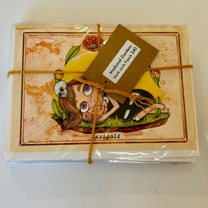 May include: A set of 9 blank cards featuring a whimsical illustration of a girl with purple eyes and a skull headband, lying on a bed of green leaves and yellow flowers. The cards are packaged in a clear plastic sleeve with a brown paper tag that reads "Medicinal Gardens blank cards 9 pack $40".