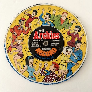 May include: A yellow vinyl record featuring a cartoon image of The Archies band. The band members are dancing and singing. The record is titled "The Archies" and includes the text "Full Fidelity" and "33 1/3 RPM". The record is a Kirshner Record.