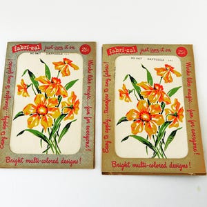 May include: Two vintage iron-on transfer sheets featuring a bouquet of yellow daffodils with green leaves. The sheets are labeled "Fabri-Cal" and "Just iron it on". The text "No. 6417 Daffodils" is printed on each sheet. The sheets are priced at 25 cents each. The text "Easy to apply...transfers to any fabric! Works like magic...fun for everyone! Bright multi-colored designs!" is printed on each sheet.