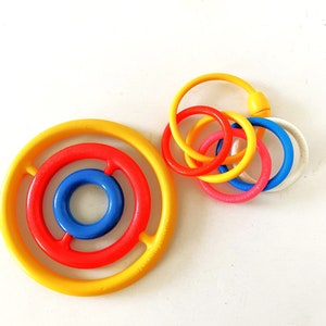 May include: A set of colorful plastic stacking rings for babies and toddlers. The rings are yellow, red, blue, and pink. The rings are designed to be stacked on top of each other, with the largest ring at the bottom and the smallest ring at the top.