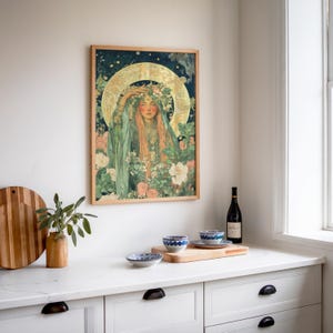 May include: A framed art print featuring a woman with long red hair, wearing a floral crown and green robes, surrounded by flowers. The artwork has a vintage style with a gold halo and a dark blue background. The frame is made of light-colored wood.