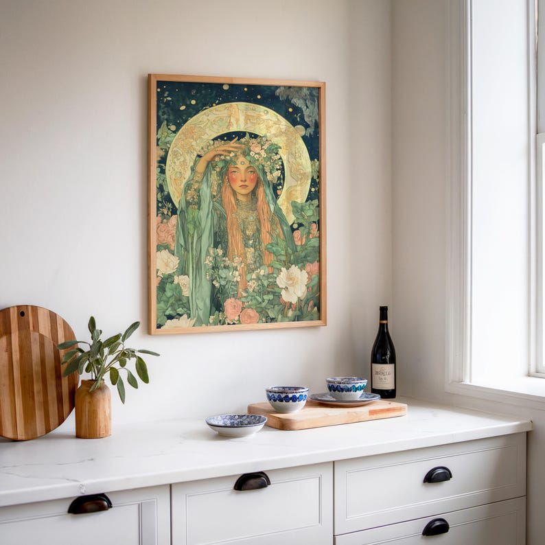 May include: A framed art print featuring a woman with long red hair, wearing a floral crown and green robes, surrounded by flowers. The artwork has a vintage style with a gold halo and a dark blue background. The frame is made of light-colored wood.