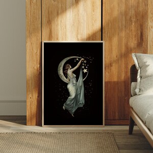 May include: A framed rectangular wall art print featuring a black background with a central illustration of a figure in a flowing light-colored gown reaching toward a crescent moon and a cluster of golden stars, surrounded by small floating light orbs.