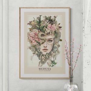 以下が含まれることがあります： 女性の顔に花と蛇が巻き付いた額縁付きのプリント。プリントの下部に「MEDUSA A GAZE SUSPENDED」というテキストがあります。