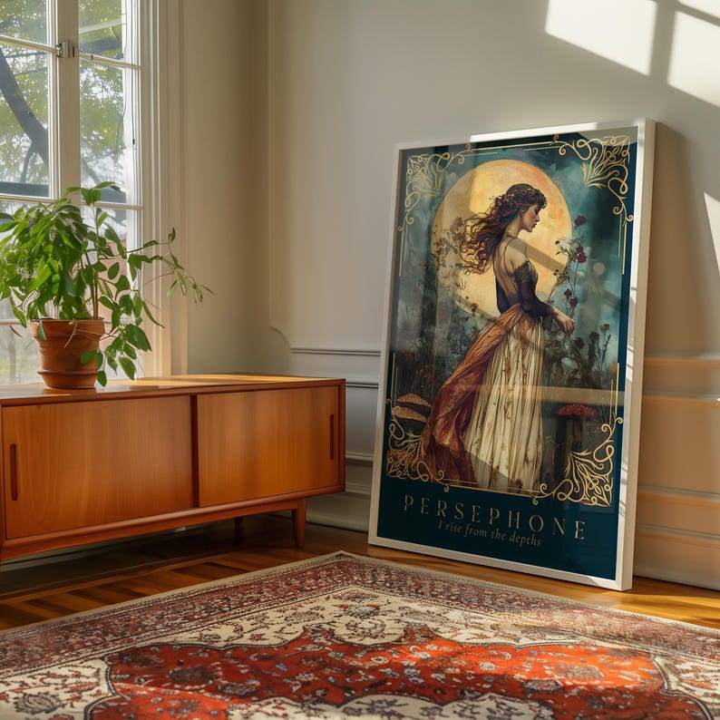 Op de afbeelding: Een ingelijste kunstdruk met een vrouw in een vloeiende jurk, tegen een achtergrond van een grote maan en bloemelementen. Het kunstwerk is ingelijst in een witte rand en bevat de tekst "PERSEPHONE I rise from the depths."