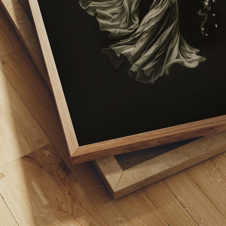 May include: A framed art print featuring a flowing, draped fabric in shades of gray against a black background. The artwork is presented in a natural wood frame, with a second frame visible beneath it. The image is set on a wooden floor.