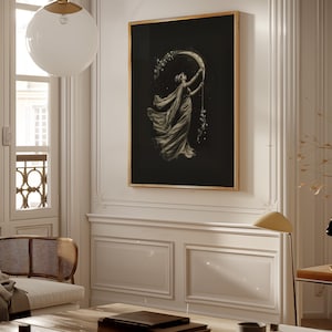 May include: A framed art print featuring a woman reaching for a crescent moon, with stars and flowing fabric. The artwork is in grayscale with a black background and a gold frame, creating a vintage aesthetic. The print is displayed on a white wall.