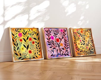 May include: Three framed floral art prints. Each features a vibrant watercolor design of flowers and foliage in a rectangular wooden frame. The color palettes include yellow, pink, and purple hues, with black leaf accents.