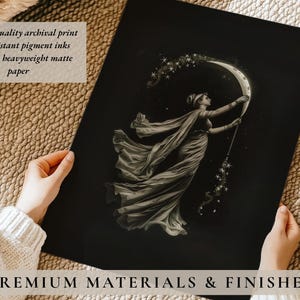 May include: A black and white print featuring a woman in a flowing gown holding a crescent moon and a star-filled wand. The print is on matte paper and includes the text "PREMIUM MATERIALS & FINISHES".