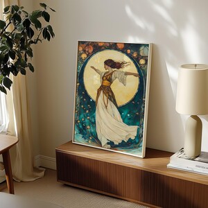 May include: A framed wall art print featuring a figure with flowing hair and arms outstretched, wearing a white and gold dress. The background displays a large, glowing yellow moon surrounded by deep teal tones and small, scattered floral elements.