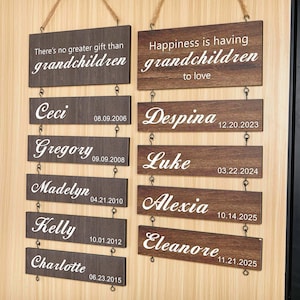 May include: Two wooden signs with the text "There's no greater gift than grandchildren" and "Happiness is having grandchildren to love". Below are individual name plaques with dates. The signs are hung with rope.