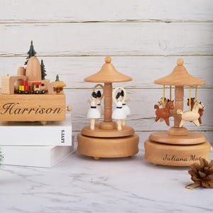 Puede incluir: Tres cajas de m&uacute;sica de madera con grabados personalizados. La primera caja de m&uacute;sica es una escena de tren con el nombre "Harrison" grabado en la parte delantera. La segunda caja de m&uacute;sica es un carrusel con cuatro figuras y el nombre "Juliana Mae" grabado en la parte delantera. La tercera caja de m&uacute;sica es un carrusel con tres caballos y el nombre "Juliana Mae" grabado en la parte delantera.