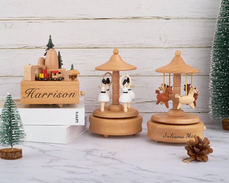 Puede incluir: Tres cajas de m&uacute;sica de madera con grabados personalizados. La primera caja de m&uacute;sica es una escena de tren con el nombre "Harrison" grabado en la parte delantera. La segunda caja de m&uacute;sica es un carrusel con cuatro figuras y el nombre "Juliana Mae" grabado en la parte delantera. La tercera caja de m&uacute;sica es un carrusel con tres caballos y el nombre "Juliana Mae" grabado en la parte delantera.
