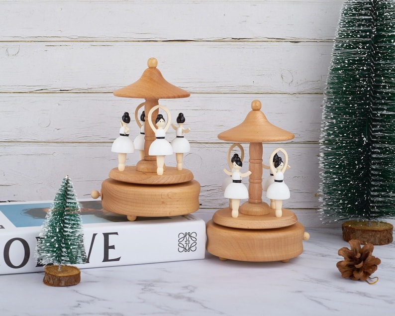 Puede incluir: Dos cajas de m&uacute;sica de madera con figuritas de bailarinas. Las cajas de m&uacute;sica est&aacute;n hechas de madera marr&oacute;n claro y tienen un dise&ntilde;o de carrusel. Las bailarinas llevan tut&uacute;s blancos y tienen el pelo negro. Las cajas de m&uacute;sica est&aacute;n sobre una superficie blanca.