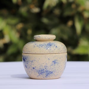 May include: A small, round ceramic jar with a lid. The jar is decorated with a speckled pattern of blue and white.