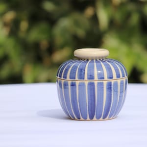 May include: A small, round ceramic jar with a lid. The jar is decorated with blue and white stripes.