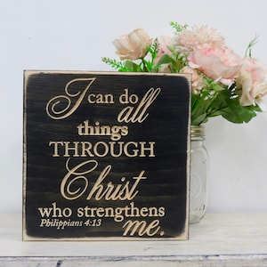 May include: A black wooden sign with white lettering that reads "I can do all things THROUGH Christ who strengthens me. Philippians 4:13"