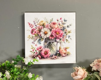 May include: Square canvas art print featuring a watercolor illustration of a floral arrangement. The bouquet, in a mason jar, includes pink roses, daisies, and other flowers. The artwork has a soft, pastel color palette, with a focus on pinks, whites, and greens.