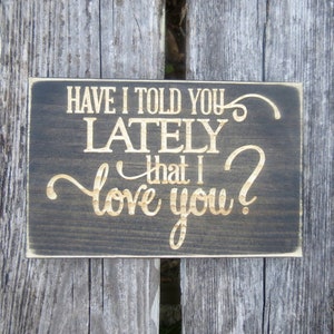 May include: A dark brown wooden sign with the text "Have I told you lately that I love you?" in gold lettering.