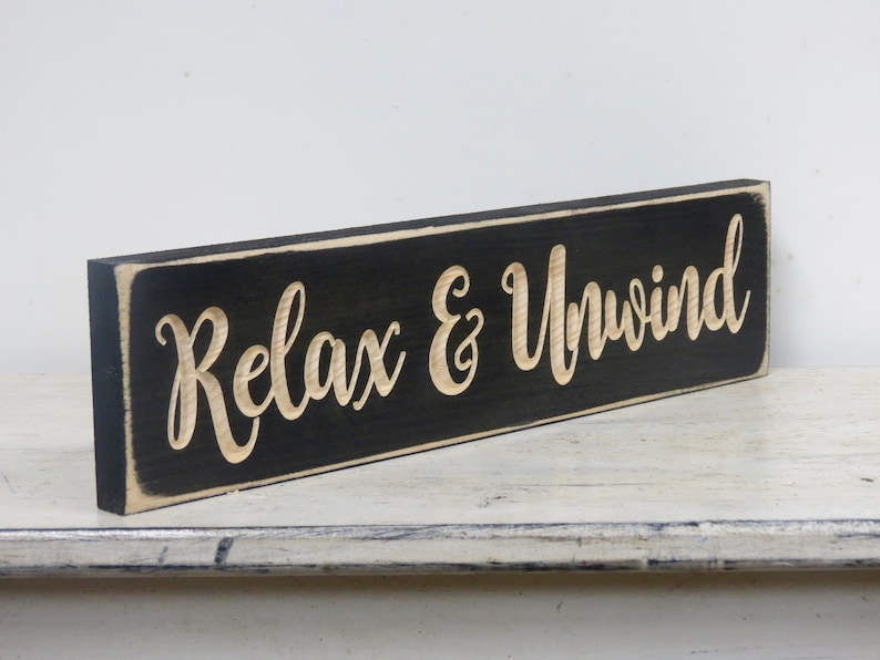 May include: Black wooden sign with white lettering that reads "Relax & Unwind".