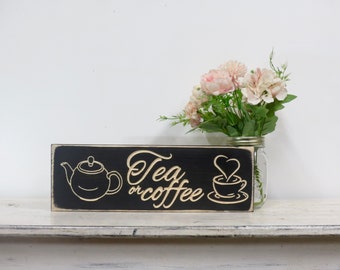 May include: Black wooden sign with white text that reads "Tea or coffee" with a white silhouette of a teapot on the left and a coffee cup with a heart-shaped steam on the right.