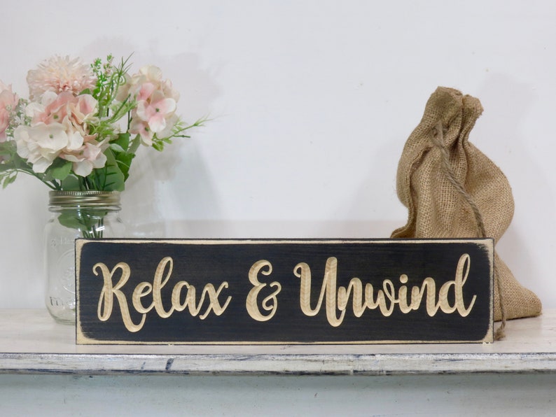 May include: Black wooden sign with white trim and the words "Relax & Unwind" in gold lettering.