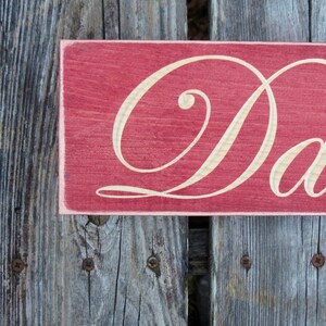 May include: A red wooden sign with the word "Dad" written in white cursive script.