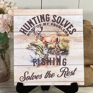 May include: A wooden sign with a rustic background featuring a deer and a fish. The sign reads "Hunting solves most of my problems, Fishing solves the rest."