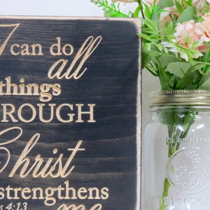 May include: A dark wood sign with the words "I can do all things through Christ who strengthens me" in gold lettering. The scripture reference "Philippians 4:13" is also included in gold lettering.